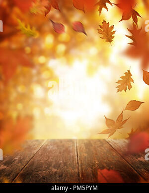 A rustic old wooden table outdoors with autumn leaves falling in the background. Stock Photo