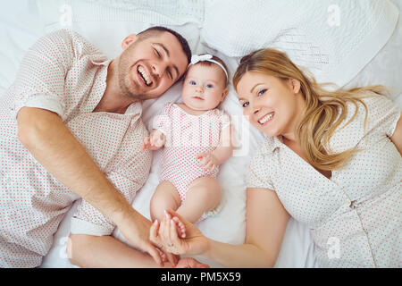 A happy family plays with a toddler on a bed in indoors. Stock Photo