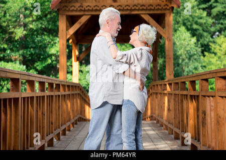 Adorable aged couple dancing while being on the bridge Stock Photo