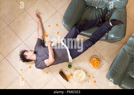 Young man after heavy partying at home. A lot of beer and junk food Stock Photo