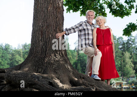 Happy pensioner touching the tree while hugging his aged wife Stock Photo