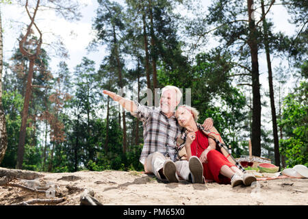 Positive pensioner pointing to the distance while sitting with his wife in forest Stock Photo