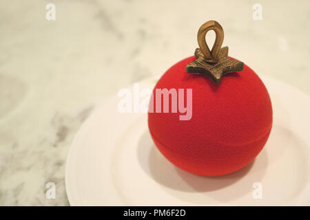 Close up of Christmas ball ornament shaped red velvet cake with berry mousse inside served on white marble table with copy space Stock Photo