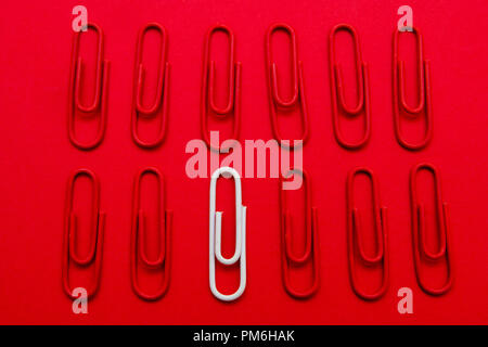 white paper clip unique concept idea on red background, stand out from the crowd. Stock Photo
