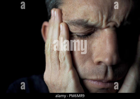 Portrait of man on black background, stressed, hands on face