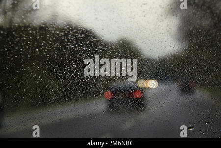 Cars with headlights on viewed through a raindrop-covered windshield. Stock Photo