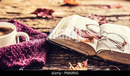 Cup of coffee old  book  glasses and autumn leaves on rustic wooden table. Stock Photo
