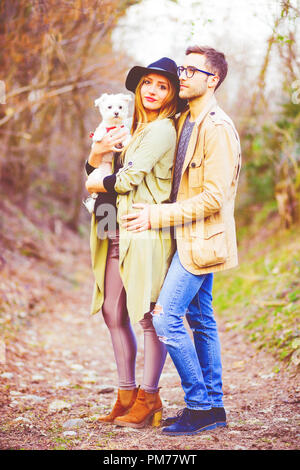 young pregnant couple posing outdoors with puppy dog - happiness, family life, quality time concept Stock Photo