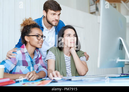 Portrait of three creative designers using computer  while collaborating on project working  at desk in office, copy space Stock Photo