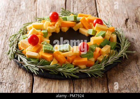 Christmas appetizer of pesto cheese, cheddar, Mimolette with tomatoes and decorated with rosemary in the form of a wreath close-up on the table. horiz Stock Photo