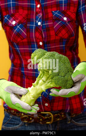 Healthy food to your table. Closeup on young woman farmer in checkered shirt on yellow background showing broccoli Stock Photo