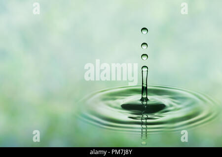 Drops of rain falling on smooth water surface. Green blurred pattern in background. Stock Photo