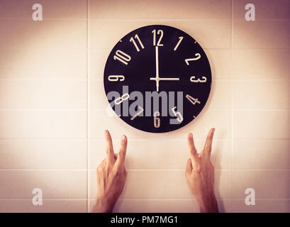 Big black clock on white wall. Time change. DST. Survey of the European Union on time change. Gesture of victory. Caucasian man. Stock Photo