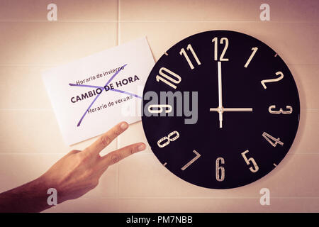 Big black clock on white wall. Time change. DST. Survey of the European Union. Gesture of victory of caucasian man.Spanish banner. Stock Photo