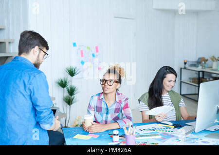 High angle portrait of contemporary African-American woman wearing glasses talking to colleagues sitting at desk in office, copy space Stock Photo