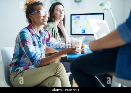 Portrait of contemporary African-American woman  wearing glasses discussing creative  project with colleagues sitting at desk in modern office, copy s Stock Photo