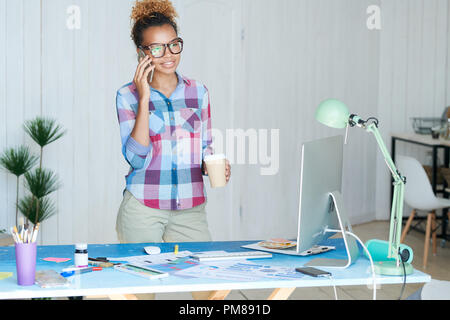Portrait of creative African-American woman speaking by phone standing by desk in modern office, copy space Stock Photo