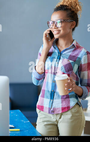 Portrait of creative African-American woman speaking by phone standing by desk in modern office Stock Photo