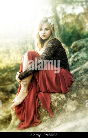 Beautiful fairy blonde dressed in a red cloth holding her legs. Stock Photo