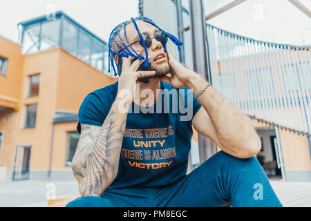 Young attractive man with blue dreadlocks talking by mobile phone and touching his hair. Stock Photo