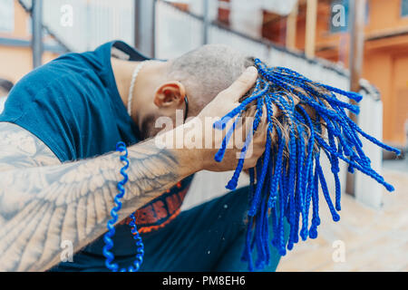 Young attractive man with blue dreadlocks touching his hair. Stock Photo