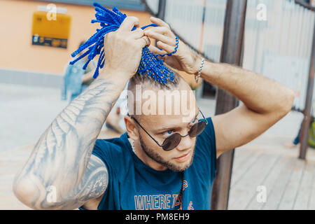 Young attractive man with blue dreadlocks touching his hair. Stock Photo