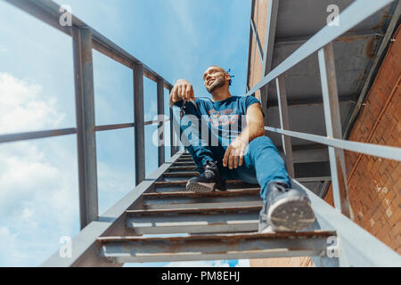 Young attractive man with blue dreadlocks sitting on staircase. Stock Photo
