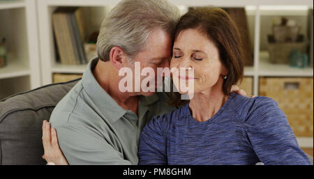 Loving senior couple cuddling on couch Stock Photo