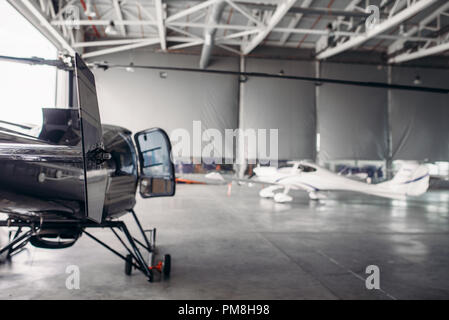 Private airline air park in airport hangar, small turboprop airplane and helicopter in aerodrome building, propeller plane and copter, inspection befo Stock Photo