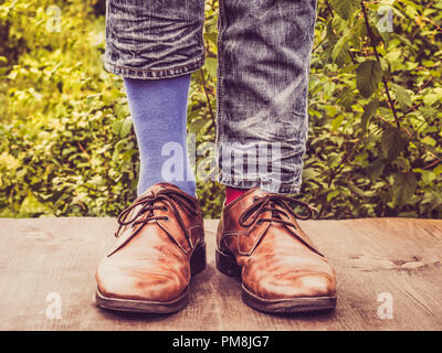 Men's legs in stylish shoes, bright, multi colored, variegated socks with Christmas and New Year's patterns on the wooden terrace on the background of Stock Photo