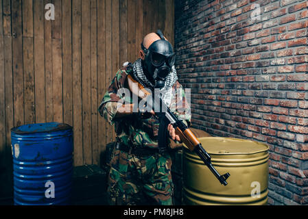 Terrorist in gas mask with kalashnikov rifle, male mujahedin with weapon. Terrorism and terror, soldier in khaki camouflage, barrels of fuel or chemic Stock Photo
