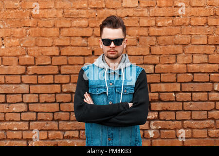 Portrait of a beautiful hipster man in a denim waistcoat near a brick wall Stock Photo