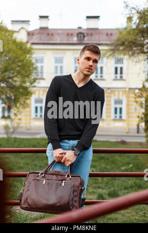Handsome young man in a black T-shirt with a leather bag, outdoors Stock Photo