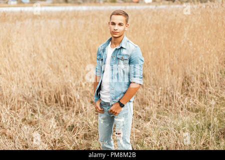 Handsome young rural man in jeans jacket and jeans walking in the field Stock Photo