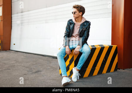 Handsome young man with a hairdo in trendy stylish clothes sits on a black-and-yellow Stock Photo
