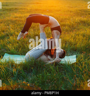 Young couple doing yoga outside the city on the grass at sunset Stock Photo