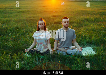 Young couple practicing yoga outdoors at sunset Stock Photo
