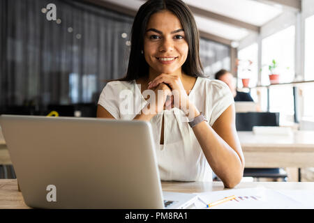 New solution every day. Confident young woman in smart casual wear working on laptop while sitting at her working place in office Stock Photo