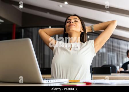 New solution every day. Confident young woman in smart casual wear working on laptop while sitting at her working place in office Stock Photo
