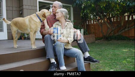 Senior couple having coffee petting dog in their yard Stock Photo