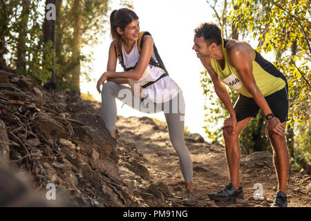 Couple taking a break while running at mountain trail race. Fit man and woman taking rest and talking during a mountain race. Stock Photo