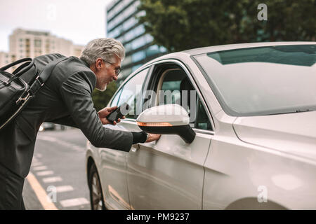 Senior man standing on road and talking to taxi driver through opened car window. Man taking a cab for traveling. Stock Photo