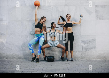 Happy women in fitness clothes having fun standing outdoors with basketball skipping rope and medicine ball. Stock Photo