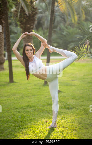 Young woman doing Yoga outdoors in park in white sportswear. Active vacation. Stock Photo