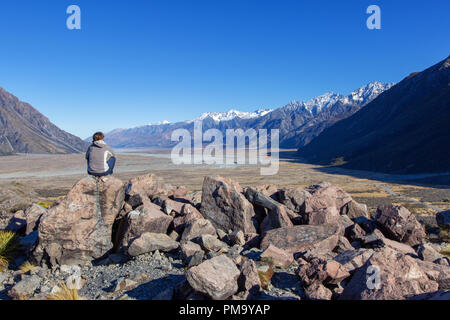 Person is sitting in Aoraki - Mount Cook Nationalpark in front of a wide valley, New Zealand, South Island Stock Photo