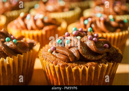 Close-up of batch of cupcakes with chocolate frosting with sprinkles on wooden board Stock Photo