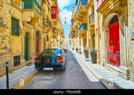 VALLETTA, MALTA - JUNE 17, 2018: The typical streetscape of Valletta with narrow pass between the tall historical buildings, decorated with colored wo Stock Photo
