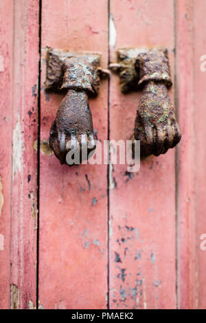 Two rusty metal hands used as door knockers on an old pink red wooden door in Portugal Stock Photo