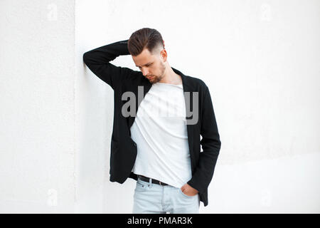 Fashionable handsome man in black stylish jacket posing near white wall Stock Photo