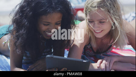 Happy group of young interracial friends looking at tech on the beach Stock Photo